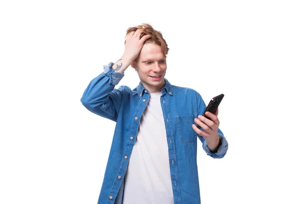 白い背景のスマートフォンを見ながら微笑んでいる若い赤毛の男 — ストック写真
