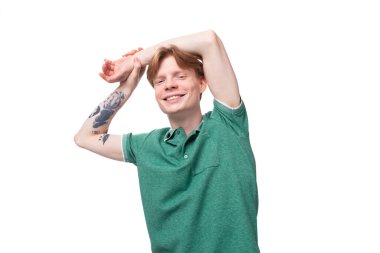 Genç, mutlu, kızıl saçlı, kolunda dövme olan Avrupalı adam yeşil bir tişört giyiyor..