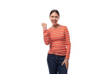 Dar turuncu bir süveter giymiş genç esmer kadın seviniyor ve yumruğunu havada tutuyor..