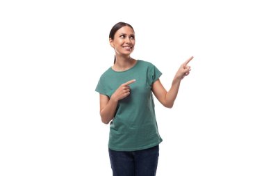 Otuz yaşında, at kuyruklu, yeşil tişörtlü esmer bir kadın parmağıyla mekanı kopyalamak için işaret ediyor. reklam kavramı.