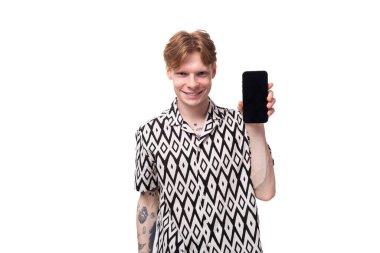 Avrupalı genç bir erkek öğrenci, kırmızı saçlı, desenli bir gömlek giymiş, akıllı bir telefonun maketli ekranını gösteriyor..