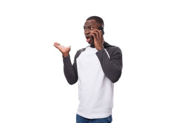 Kısa saçlı, uzun kollu bir kazak giyen Afrikalı genç bir adam akıllı telefon kullanarak kızıyor..