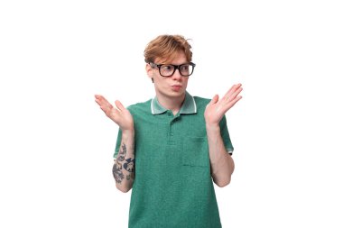 Genç, beyaz, kırmızı saçlı, yeşil tişörtlü bir adam cehaletle omuzlarını silkiyor..