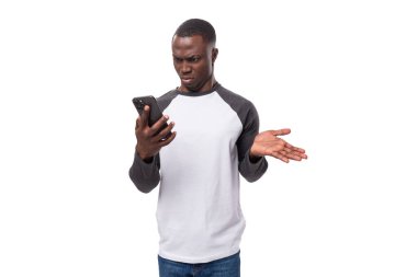 Kısa saçlı, uzun kollu bir kazak giyen Afrikalı genç bir adam akıllı telefon kullanarak kızıyor..