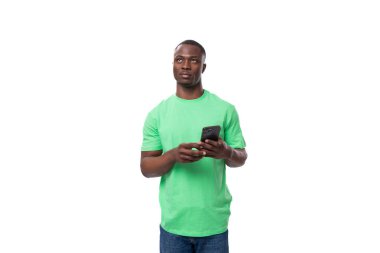 Genç, şaşkın, yeşil tişörtlü Amerikalı adam akıllı telefon kullanıyor..