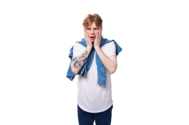 Genç, yakışıklı, ince, kızıl saçlı, kollarında dövme olan adam şık bir mavi gömlek giyiyor..