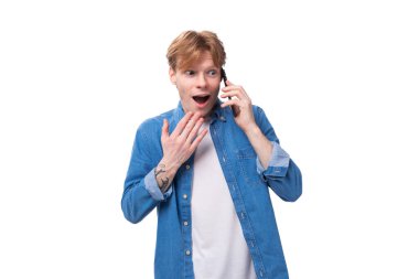 Mavi gömlekli, kızıl saçlı genç bir adam telefonda bir sır söylüyor..