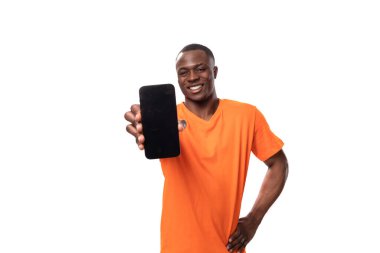 Turuncu tişört giyen genç Afrikalı adam akıllı telefon ekranı gösteriyor..
