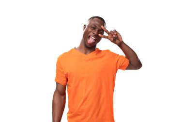 Turuncu tişört giymiş genç, bakımlı, Afrikalı bir adam yüzünü buruşturuyor ve dilini gösteriyor..