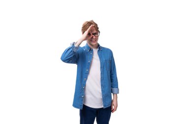 Genç, kızıl saçlı, mavi tişörtlü adam beyaz arka planda gözlük takıyor ve fotokopi çekiyor..