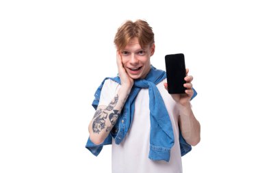 Mavi kot gömlekli, gülümseyen kızıl saçlı genç bir adam akıllı telefon ekranının bir maketini gösteriyor. reklam kavramı.