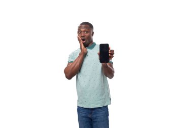 Genç, cana yakın, kısa saçlı, yaz tişörtü giymiş Amerikalı bir adam ve sürpriz bir şekilde kot pantolon giymiş bir cep telefonunun maketini gösteriyor..