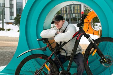 Gri ceketli ve siyah şapkalı beyaz bir adam dışarıda bisikletle vakit geçiriyor..