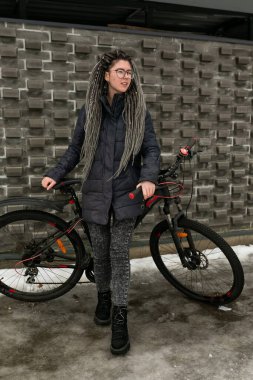 Sarı saçlı, kışlık ceketli, sevimli genç bir kadın bisiklet sürüyor..