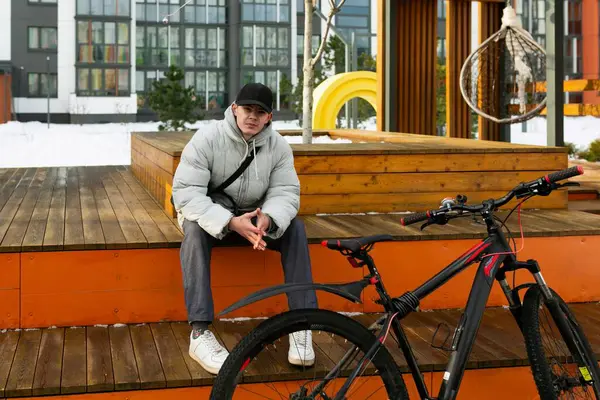Sonbahar elbiseli genç bir adam bisiklet sürdükten sonra dinlenmek için oturdu..