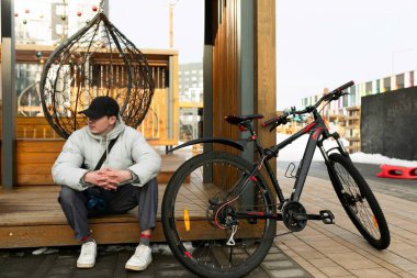 Şapkalı ve ceketli bir adam kiralık bisikletle ayakta duruyor..