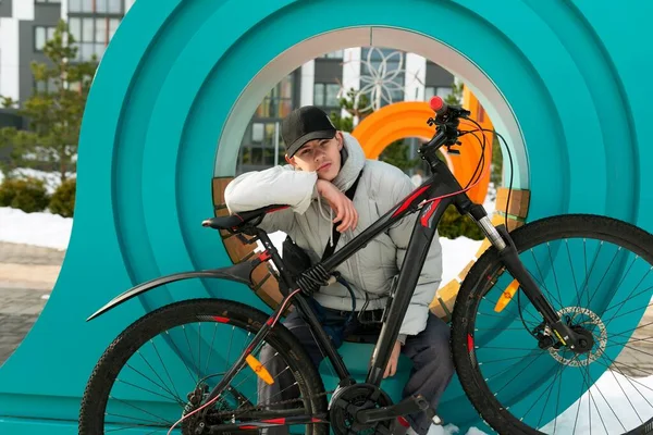 Şapkalı ve ceketli bir adam şehirde bisikletli bir yürüyüşün tadını çıkarır..