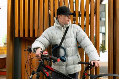 Sonbahar kıyafetleri içinde, sokakta bisiklet taşıyan bir omuz çantası olan genç adam..