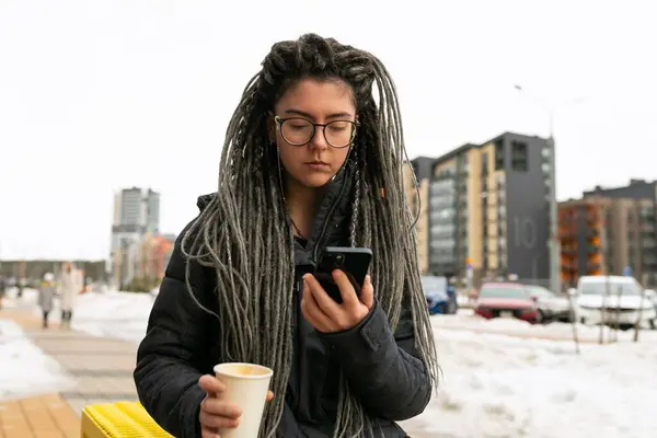 Photo on the street, young pretty informal woman wears dreadlocks hairstyle.