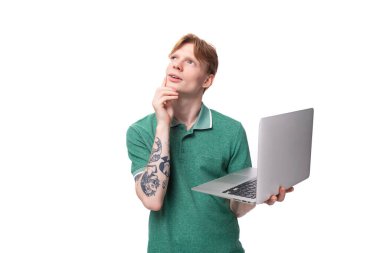 Yeşil tişörtlü akıllı, sevimli, kızıl saçlı adam çalışmak ve çalışmak için dizüstü bilgisayar tutuyor..