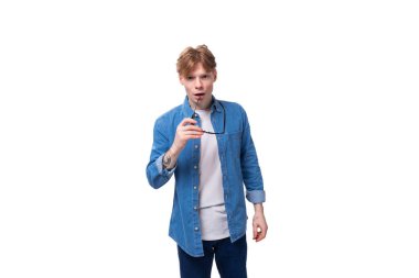 Bakır saçlı, genç, Avrupalı bir adam. Kot gömlek giyiyor. Gözlük takıyor..