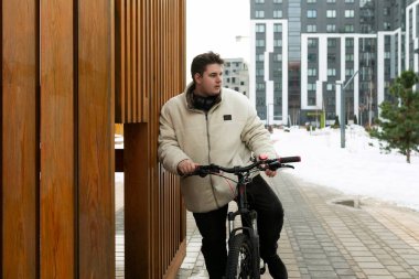 Kışlık ceketli genç Avrupalı bir adam bisikletle şehirde dolaşıyor..