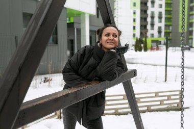 Kışlık ceketli genç ve güzel bir kadın oyun alanında yürürken havanın tadını çıkarıyor..