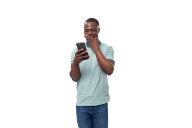 Kısa saçlı, temiz tişörtlü ve kot pantolonlu yakışıklı Afrikalı bir adam sosyal ağlarda akıllı telefondan iletişim kuruyor..