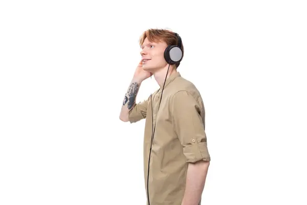 stock image young red-haired guy in glasses and a brown shirt listens to music on headphones.