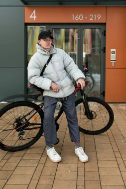 Şapkalı bir adam evin avlusunda bisikletle duruyor..