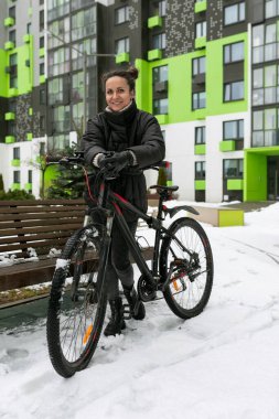 Siyah ceketli güzel bir kadın evinin yanında bisikletle yürüyor..