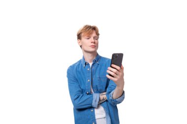 Kot gömlekli, beyaz saçlı genç bir adam akıllı bir telefona şaşkınlıkla bakıyor..