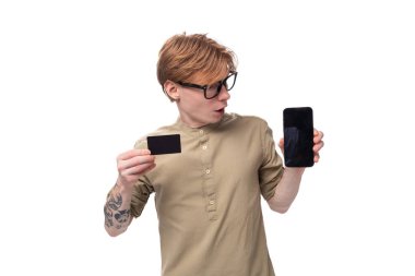 Kızıl saçlı, kolunda haki rengi tişört olan yakışıklı, beyaz bir erkek tanıtımcı. Plastik bir kartın tanıtımını yapıyor. e-ticaret.