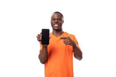Kısa saçlı, turuncu tişörtlü genç bir Amerikalı beyaz arka planda akıllı bir telefonun reklamını yapıyor..
