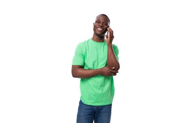 Açık yeşil tişörtlü ve kot pantolonlu Afrikalı genç adam telefonda konuşuyor..