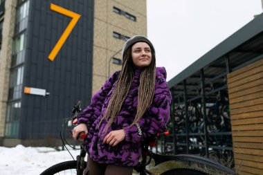 Rastalı ve piercingli Avrupalı bir kadın bisikletle şehirde dolaşıyor..