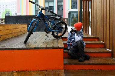 Kışlık ceket giymiş beyaz bir çocuk şehirde bisikletle dolaşıyor..