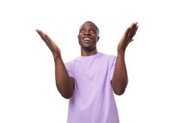 Hafif bir tişört giymiş genç ve enerjik bir Amerikalı. Fotokopi alanı olan beyaz bir arka planda gülüyor..