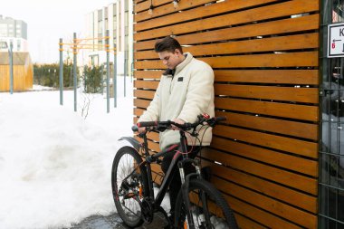 Kışlık ceket giymiş genç Avrupalı bir adam bisiklet sürüyor..