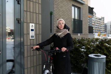 Kışın giyinmiş genç bir kadın bisikletle şehirde dolaşıyor..