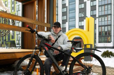 Şapkalı ve ceketli bir adam bankta bisikletle dinlenmek için oturdu..