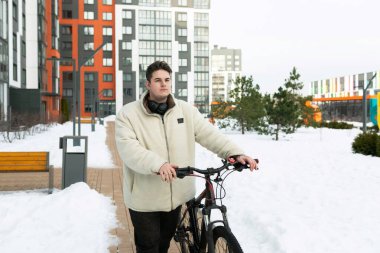 Kışlık ceket giymiş genç Avrupalı bir adam bisiklet sürüyor..