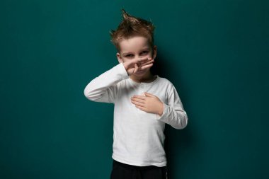 Genç bir çocuk canlı yeşil bir duvarın önünde duruyor, merakla kameraya bakıyor. Oğlan gündelik kıyafetler giyiyor ve şehir ortamında gibi görünüyor..