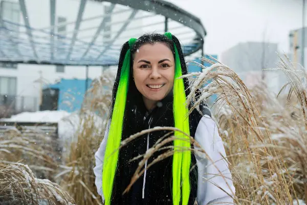 stock image A woman with vibrant green hair is standing confidently in the middle of a field, her long hair flowing freely in the wind. She gazes ahead with a determined expression, surrounded by the tall grass