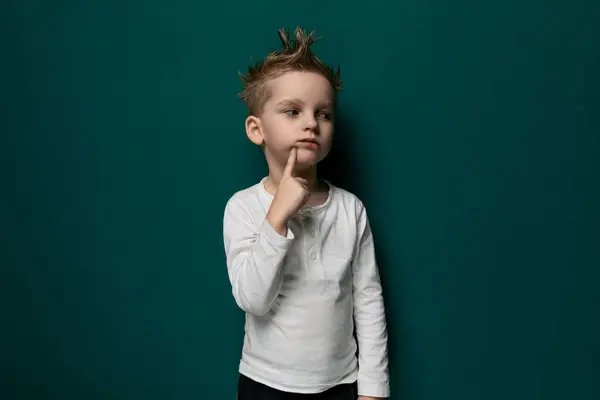 stock image A young boy is standing alone against a vibrant green wall, looking straight ahead. He is wearing casual clothes and appears to be deep in thought.