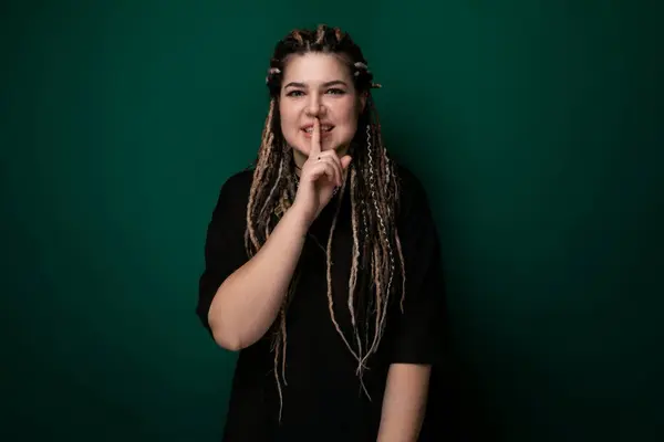 stock image A woman with long dreadlocks is standing in front of a green wall. She appears confident and stylish, showcasing her unique hairstyle.