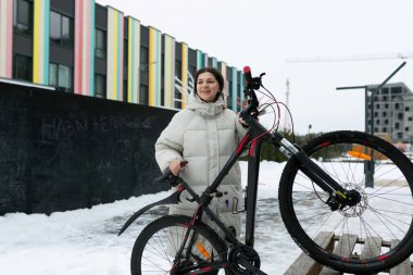 Karla kaplı bisikletinin yanında bir kadın duruyor. Ana konu motorla karlı bir kış günü çekiliyor..