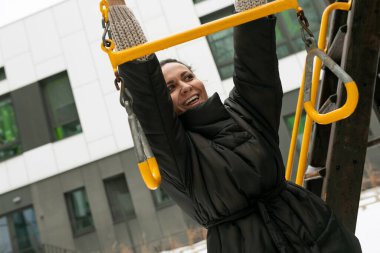 Hoş esmer, rahat kıyafetler giyip salıncaklı bir oyun alanında eğleniyor..