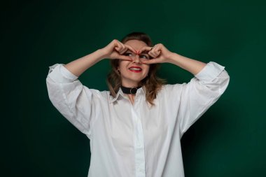 Bir kadın ellerini göğsünün önünde kaldırmış, parmaklarıyla kalp şeklinde duruyor. Sevginin ve sevginin sembolünü yaratırken gülümsüyor..