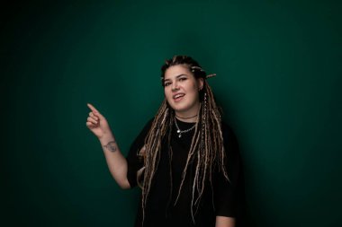 Rasta bukleli bir kadın kameranın dışındaki bir şeyi işaret ediyor. Bir sohbete dalmış ya da özel bir nesneye dikkat çekiyor gibi görünüyor. Yüz ifadesi odaklandığını gösteriyor.